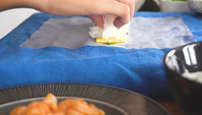 Assemble spring rolls: Lay rice paper flat, add noodles, vegetables, and herbs.