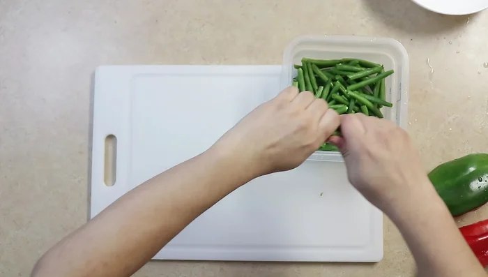 Cut string beans into 2-inch pieces. Slice red and green bell peppers. Mince garlic and slice the onion.