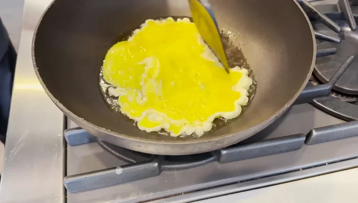 Gently lift the edges of the omelette with a spatula, tilting the pan to allow uncooked egg to flow underneath.