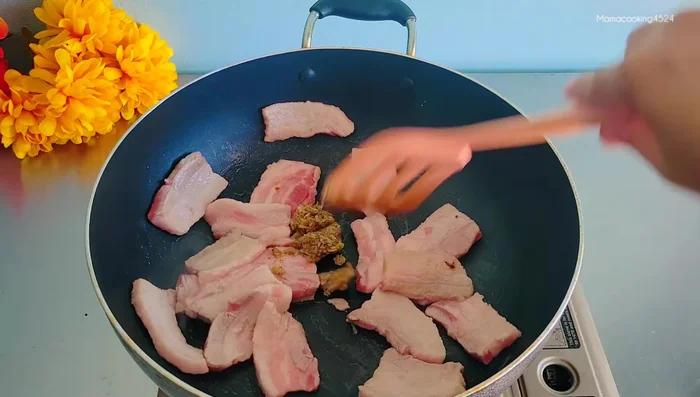 Add aromatics: Add crushed garlic and pepper (or coriander root) to the pork belly and stir-fry until fragrant.
