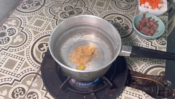 Put water in a pot and heat it over medium heat. Add 1 soup cube and dried shrimp. Add dried squid.