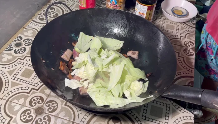 Gradually add the cabbage to the pan, stir-frying until wilted. Add banana blossom and stir-fry until slightly charred.