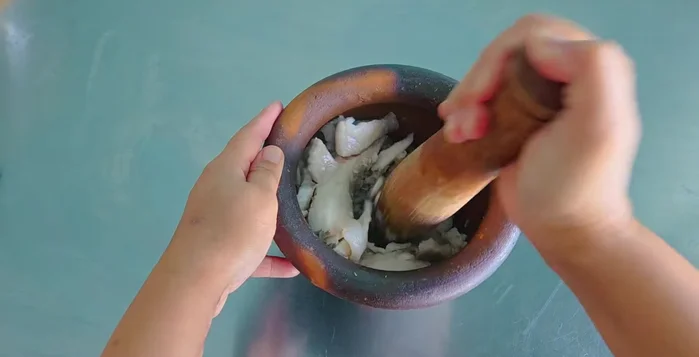 Pound the cooked tilapia meat in a mortar and pestle until fluffy.