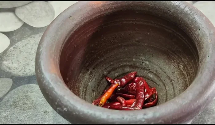 Prepare the aromatics: Pound fresh red chilies and 5 cloves of garlic until finely minced.