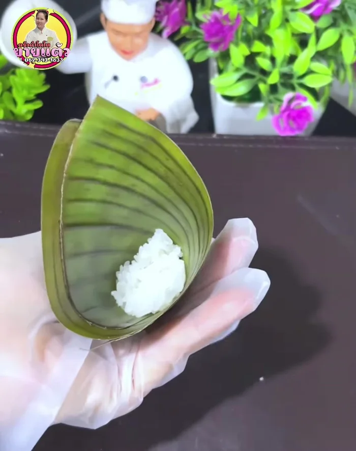Assemble the sticky rice parcels: Place sticky rice, banana slices, and more sticky rice in the center of a banana leaf. Wrap tightly and secure with toothpicks.