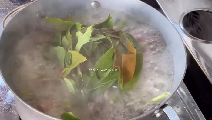Tear the cha-om leaves into small pieces and add them to the pot.
