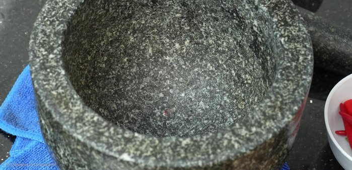 Pound garlic, coriander root, pepper, and peppercorns in a mortar and pestle.