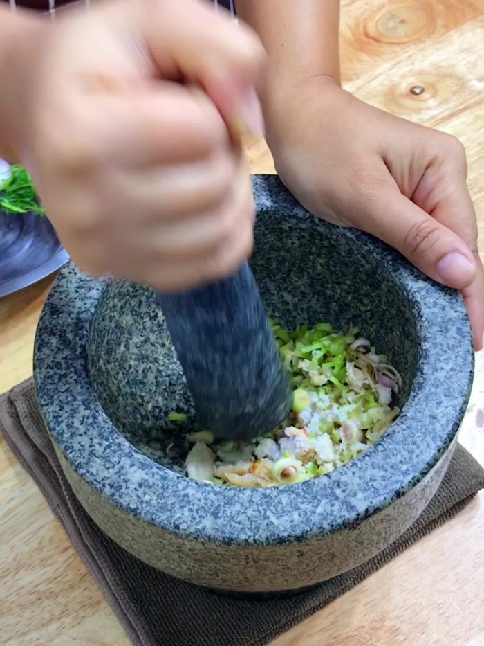 Add dried chilies, fresh red chilies, and makrut lime leaves to the mortar and pestle; pound roughly. (16.88)