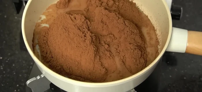 Heat the mixture over low heat in a flat-bottomed pan, stirring continuously. This helps dissolve the cocoa and creates a thicker consistency.