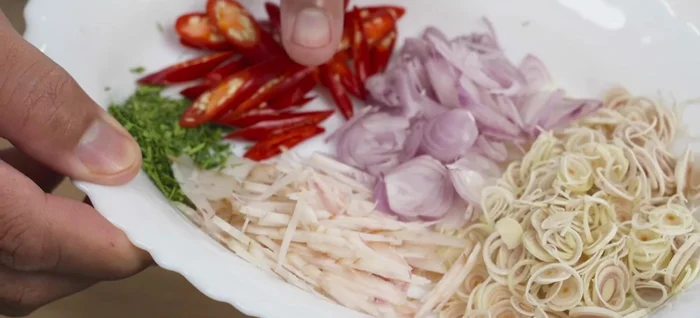 Prepare steaming cups: Place finely chopped Tom Yum herbs (galangal, lemongrass, shallots, kaffir lime leaves) at the bottom of steaming cups.