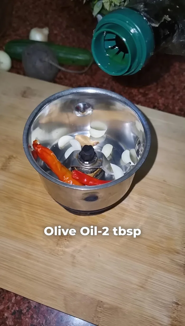 Add two dried red chilies, one piece of ginger, eight to nine garlic cloves, two tablespoons of olive oil, and fresh mint leaves to a grinding jar. Grind coarsely.