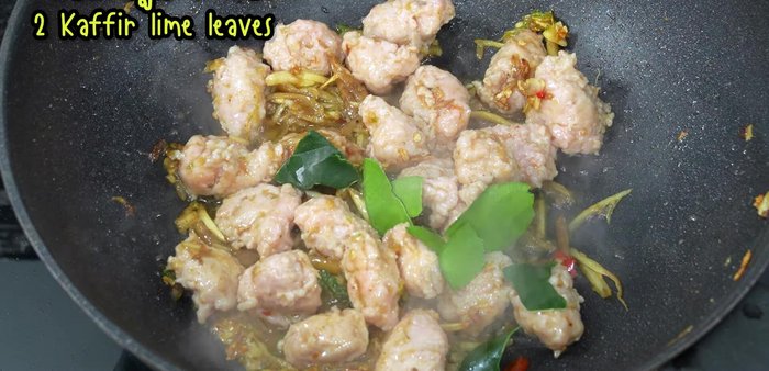 Add torn kaffir lime leaves, young peppercorns, yellow chili, and red chili. Stir-fry until chilies wilt.