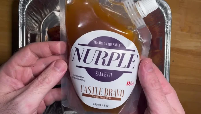 Transfer the pork belly to a tin foil pan. Coat generously with Nerple Sauce Co. Castle Bravo sweet Thai chili sauce.