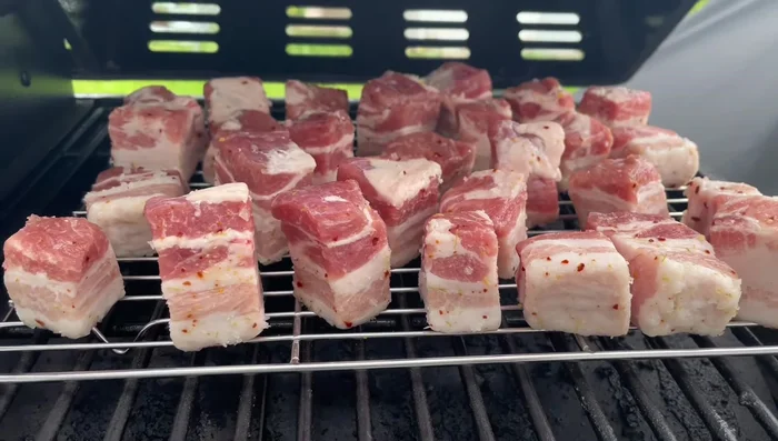 Smoke the pork belly at 250-300°F (121-149°C). At around the 1-hour mark, spritz with apple cider vinegar or your preferred liquid (apple juice, orange juice, water, or beer).