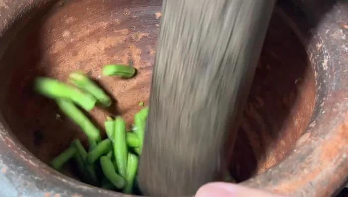 Pound the long beans in a mortar and pestle until soft.