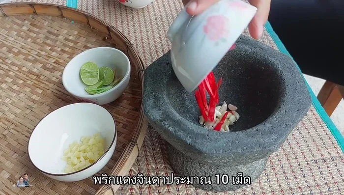 While the chicken cooks, prepare the dipping sauce. Peel and prepare 1 head of Thai garlic, 10 red chili peppers, and 2 coriander root stalks. Pound them together until fine.