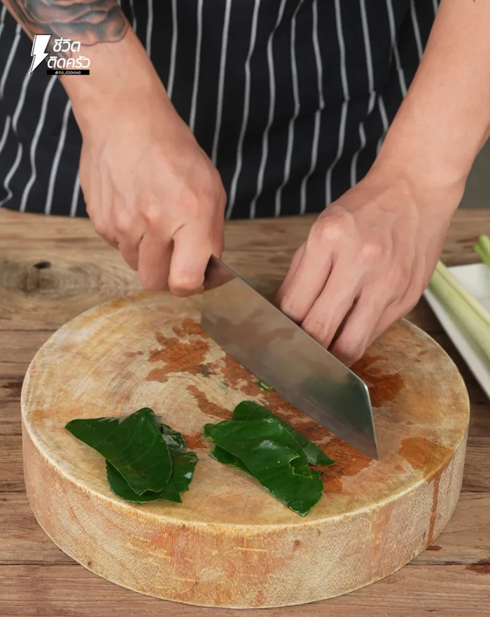 Collect and wash kaffir lime leaves from the garden. Pick only the leaves, roll them, and chop into thin strips.